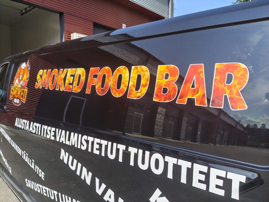 Pakettiauton kyljessä värilliset mainostekstit ja tunnus.